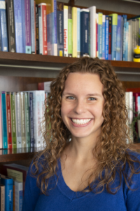 Photo of Cassie Shriver in front of a book case filled with books.